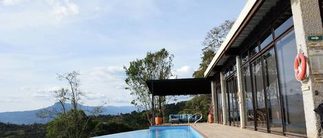 An infinity pool with a clear view of the mountains in the background, a covered seating area, and a lifebuoy attached to the building.