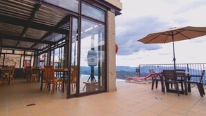 Une terrasse extérieure avec des tables et des chaises, une paroi en verre et une vue sur les montagnes.