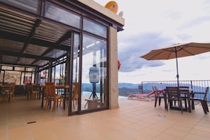 Une terrasse extérieure avec des tables et des chaises, une paroi en verre et une vue sur les montagnes.