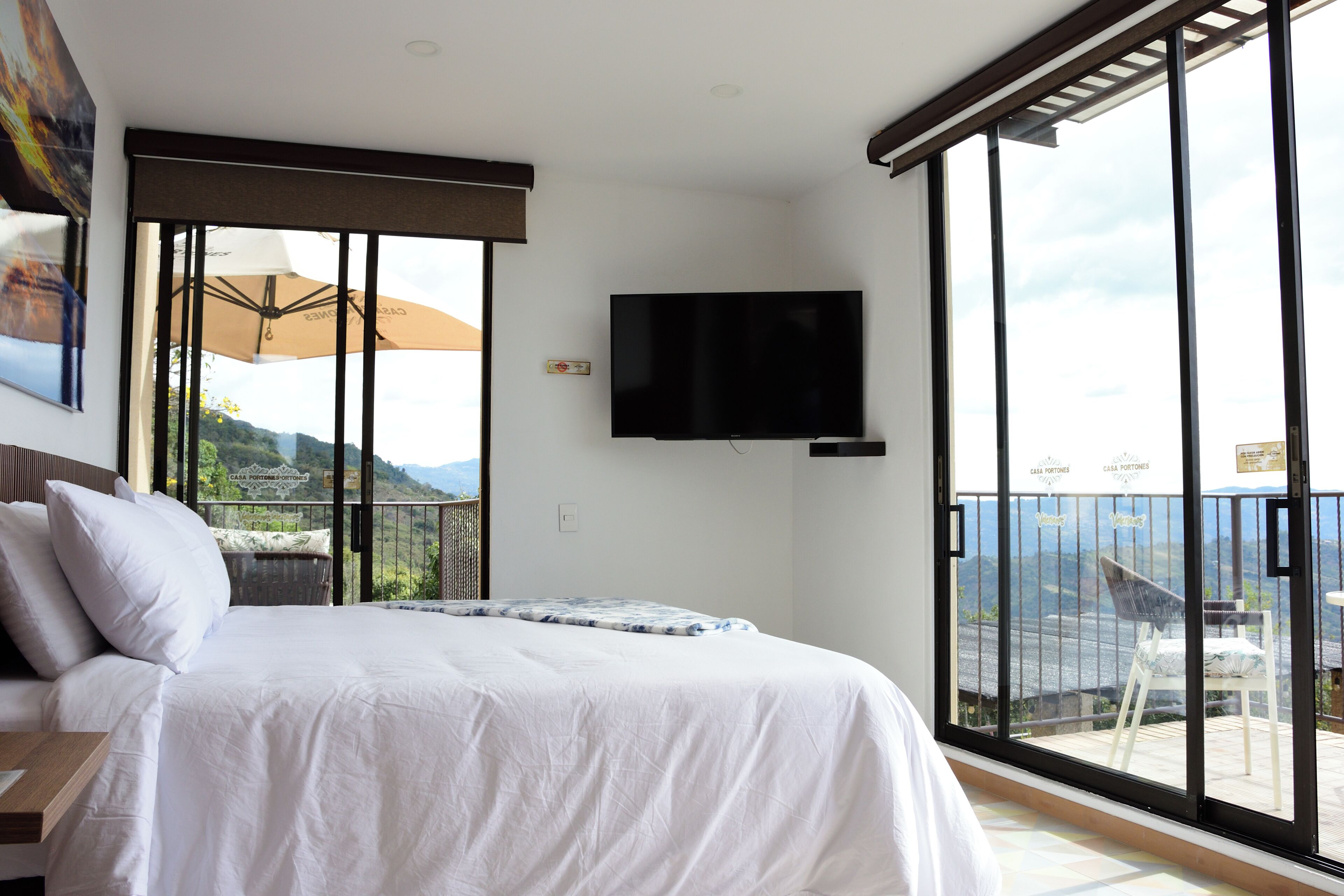 Habitación de hotel con cama, televisión de pantalla plana y balcón con vistas a las montañas.