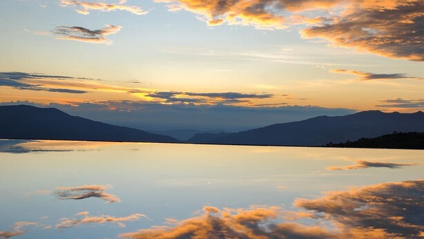A serene landscape with a calm lake reflecting the sky and mountains in the distance. - Hotel Casa Portones  (San Bernardo)