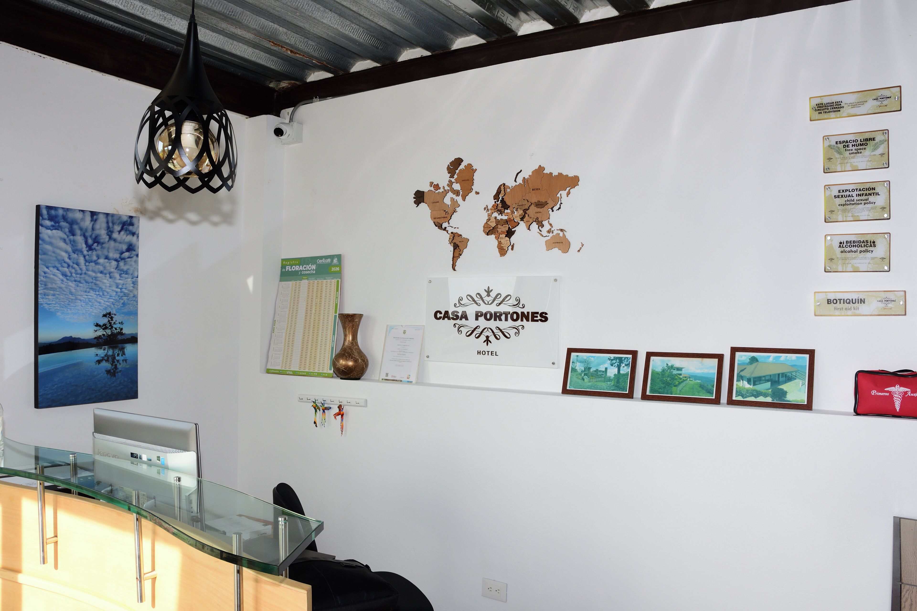 Quarto de hotel com um mapa-múndi, um certificado emoldurado, um vaso e quadros nas paredes.