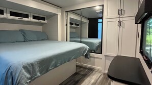 A compact bedroom with a bed, a small kitchenette, and a mirrored closet.