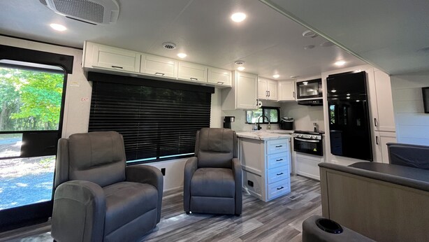 A modern RV interior with a kitchen, seating area, and a large window.