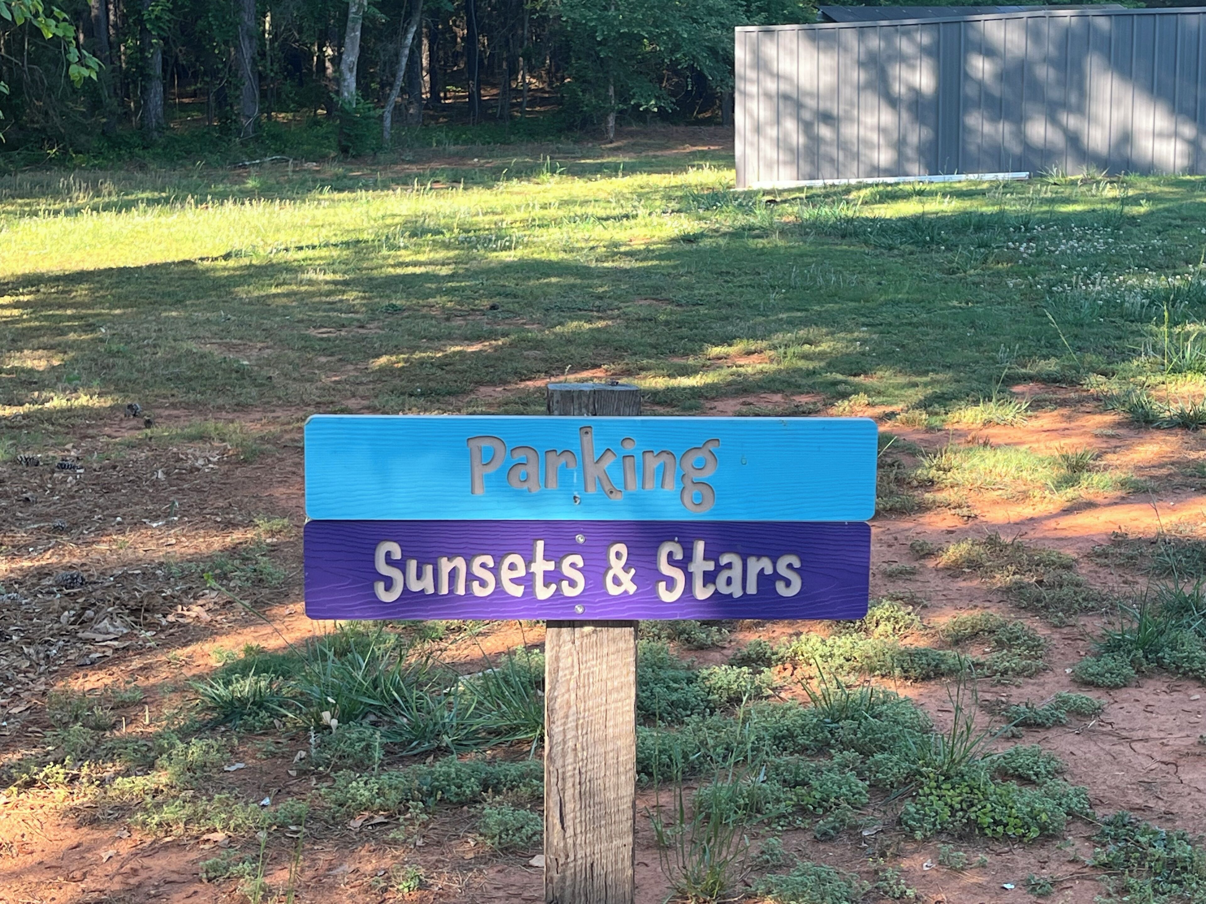 Un panneau en bois sur lequel est écrit « Parking » et « Couchers de soleil et étoiles ».