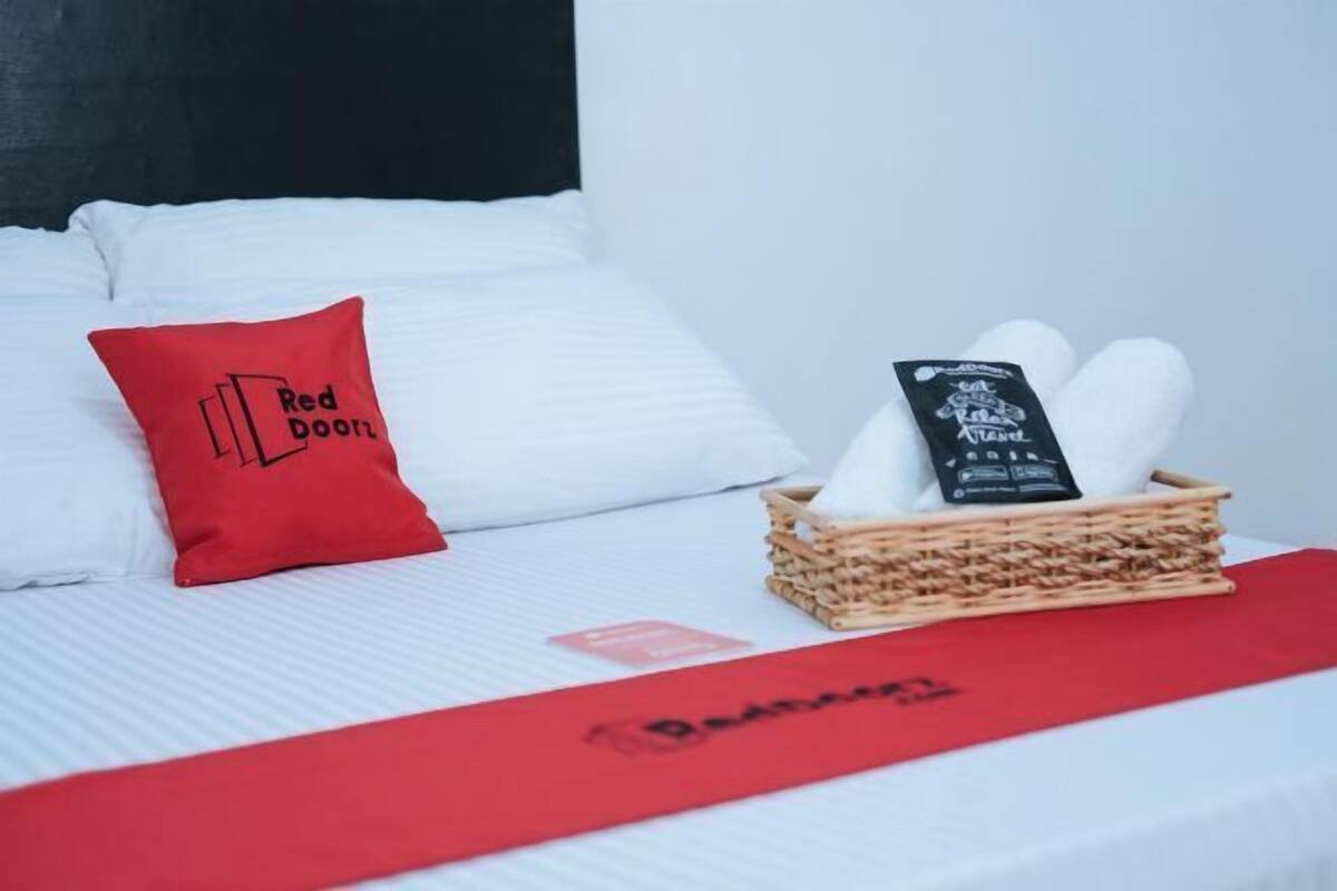 Hotelkamer met een bed, een rood kussen met de tekst 'Red Door', een mand met handdoeken en een rode bedspreider.