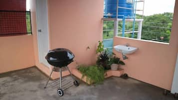 A small balcony with a barbecue grill, a sink, and potted plants.