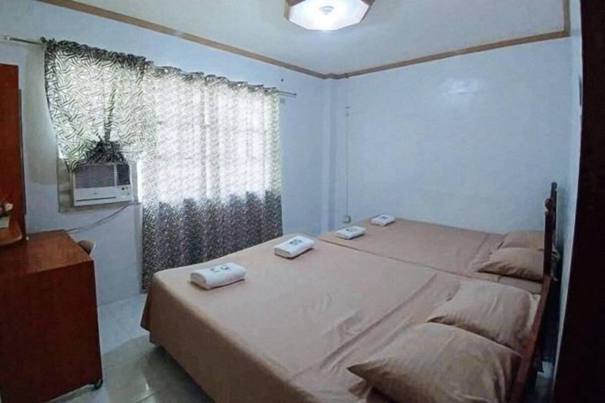 Een kamer met twee bedden, een bureau, een raam met patroon gordijnen en een plafondlamp.