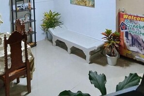 Una habitación con una mesa de comedor, sillas, un banco, plantas en macetas y un cartel de bienvenida.