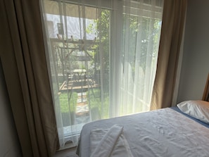 A bedroom with a bed, a window with curtains, and a view of an outdoor patio area.