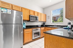 A modern kitchen with wooden cabinets, stainless steel appliances, and a black countertop.