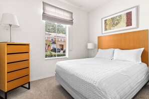 A hotel room with a bed, a wooden dresser, a window with blinds, a wall-mounted lamp, and a framed picture. - Peaceful/4 mi to Disney/Gated/Pool/Waterslides (kissimmee)