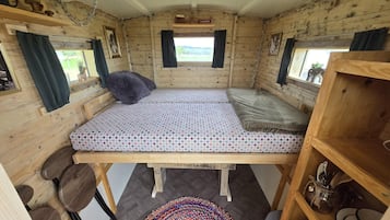 A cozy cabin-style room with a bed, a small table, and a shelf with various items.
