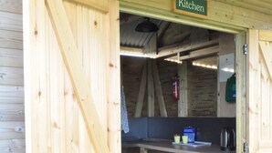 A wooden kitchen with a sign labeled "Kitchen," a small refrigerator, a sink, and a coffee maker. - Restored Circus Wagon (Saltburn-by-the-Sea)