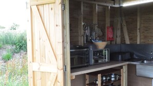 A rustic wooden kitchen with a sign labeled "Kitchen," a built-in microwave, and a sink. - Restored Circus Wagon (Saltburn-by-the-Sea)
