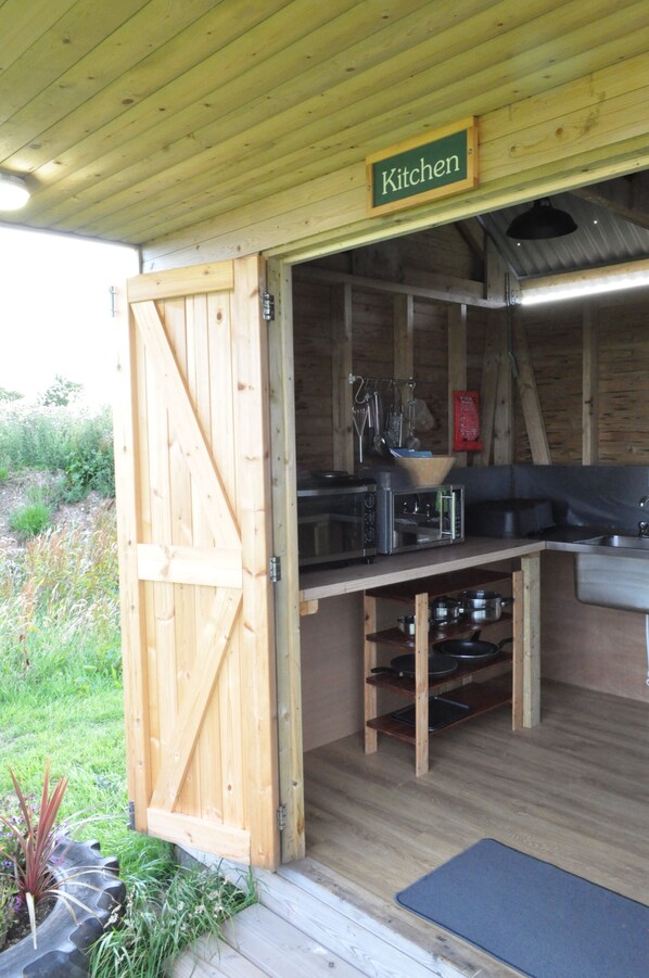A rustic wooden kitchen with a sign labeled "Kitchen," a built-in microwave, and a sink. - Restored Circus Wagon (Saltburn-by-the-Sea)