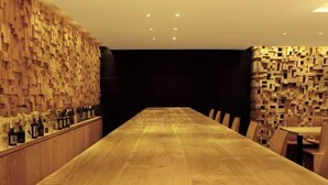 A long wooden table with chairs, a bar area with bottles, and a patterned wall. - One Eleven Retreat (Bali)