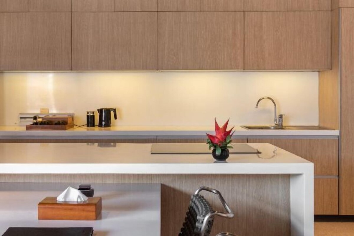 A modern kitchen with wooden cabinets, a white countertop, a sink, and a vase with red flowers.
