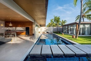 Un espace piscine moderne offrant une vue dégagée sur la piscine, un bar et un espace extérieur couvert.