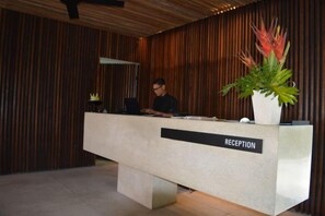 Vastaanottotiski, jossa on kyltti, jossa lukee ”RECEPTION”, kannettava tietokone ja ruukussa oleva kasvi.