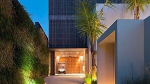 A modern building with a car parked in front, a pathway leading to the entrance, and a well-lit interior. - One Eleven Retreat (Bali)