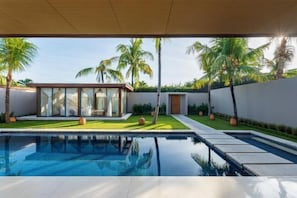 Un espace piscine moderne offrant une vue dégagée sur une structure entièrement vitrée, des palmiers et une pelouse bien entretenue.