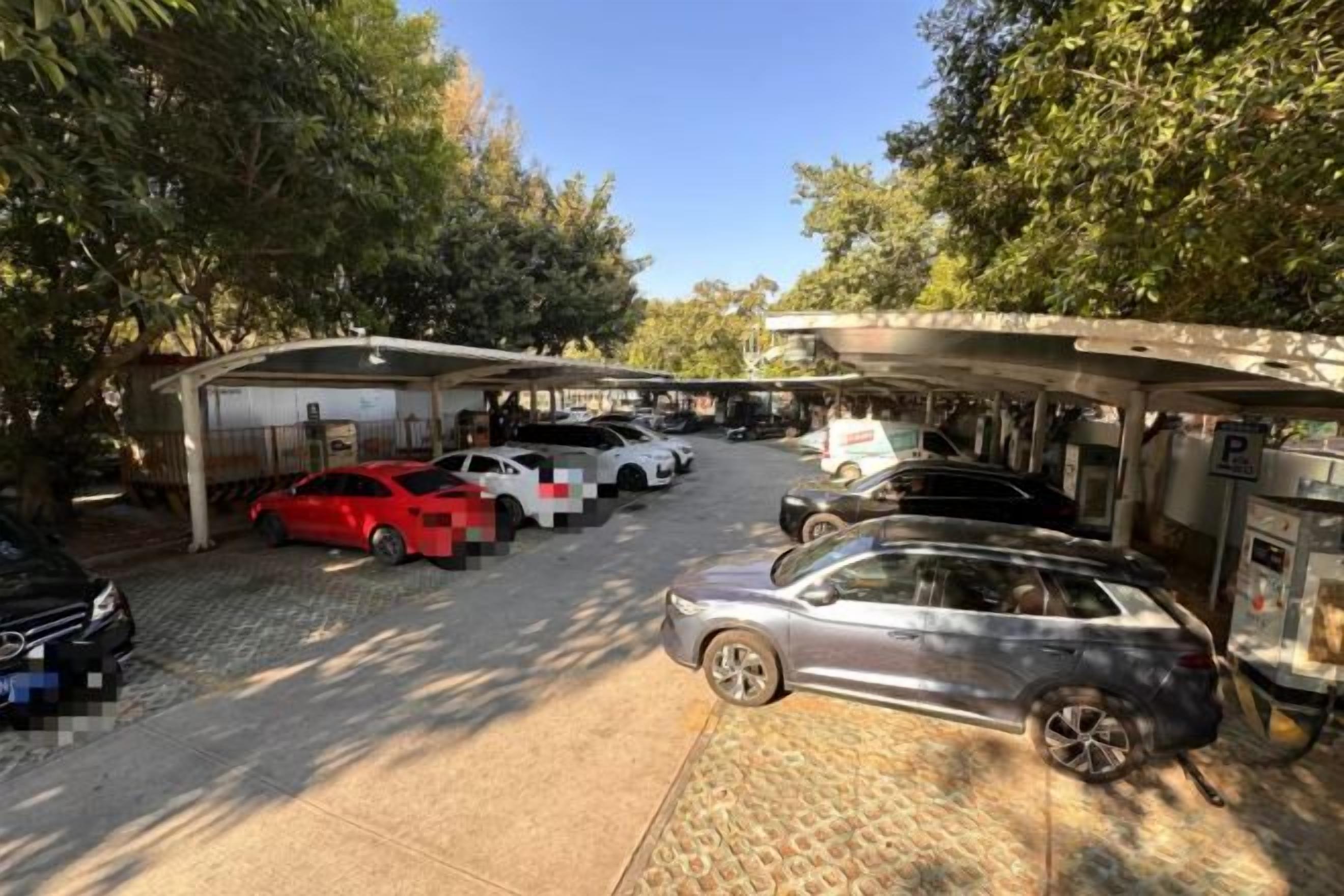 Ein Parkplatz mit mehreren Autos, überdachten Parkgebäuden und Bäumen.