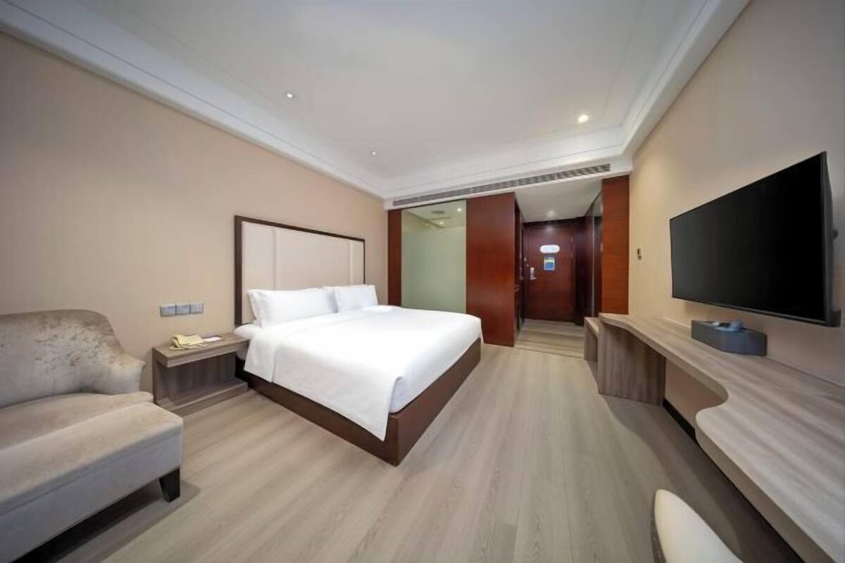 Ein modernes Hotelzimmer mit einem großen Bett, einer Sitzecke, einem Fernseher und einem Schreibtisch.