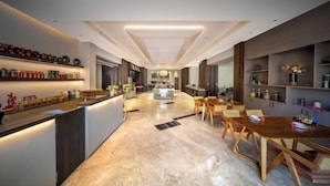 A modern hotel lobby with a central reception desk, a dining area with wooden tables, and a kitchen visible in the background. - Vanilla Garden Hotel (Xiamen)