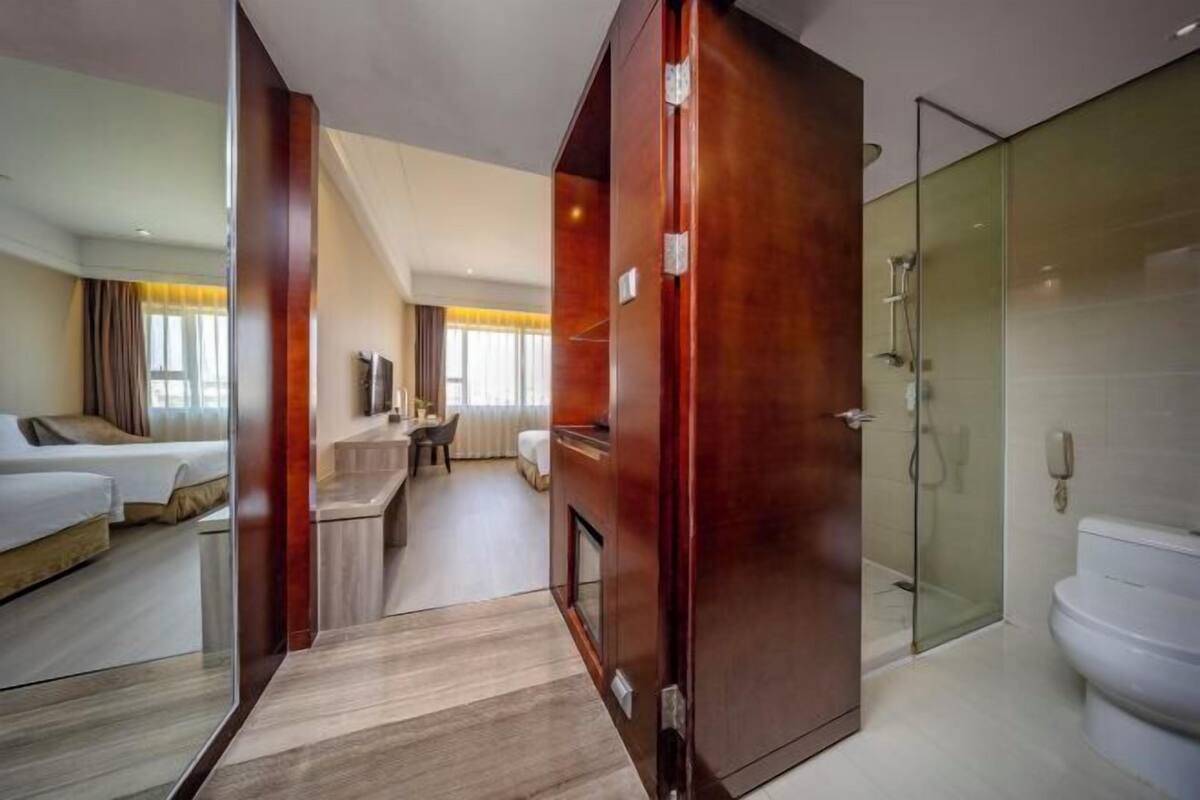Ein Hotelzimmer mit Bett, Schreibtisch, Stuhl, einer Couch, einer Duschkabine aus Glas und einer Toilette.