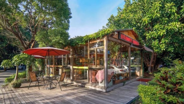 A glass-fronted building with a wooden deck, outdoor seating, and lush greenery. - Vanilla Garden Hotel (Xiamen)