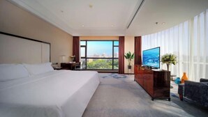 A hotel room with a large bed, a TV, a desk, and a view of the city through large windows. - Vanilla Garden Hotel (Xiamen)