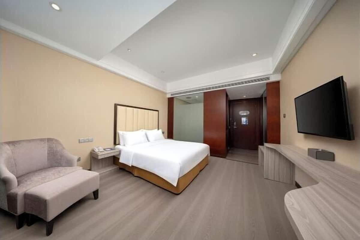 Ein Hotelzimmer mit einem Bett, einem Sessel, einem Schreibtisch, einem Fernseher und einem Spiegel.
