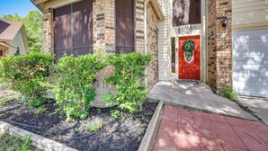 A two-story house with a red door, brick exterior, and a small garden area with mulch and plants. - Spacious San Antonio Home: Google Fiber, Game Room (San Antonio)