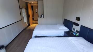 A hotel room with two beds, a small table with a phone and a cup, and a wall-mounted TV.
