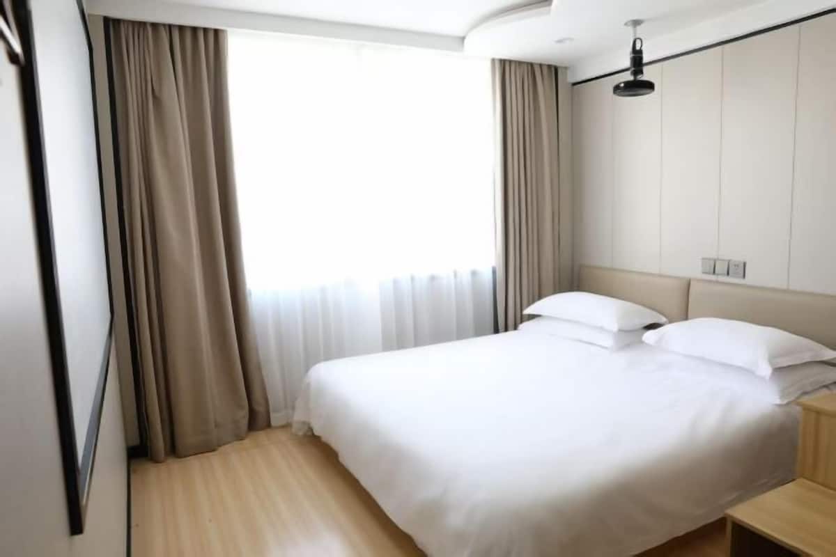 Una camera d'albergo con un letto, tende, un comodino e una lampada a soffitto.