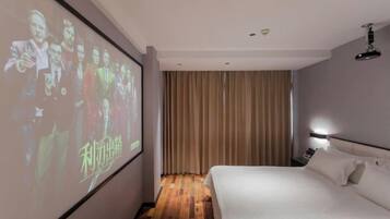 A hotel room with a bed, a projector screen, curtains, and a nightstand.
