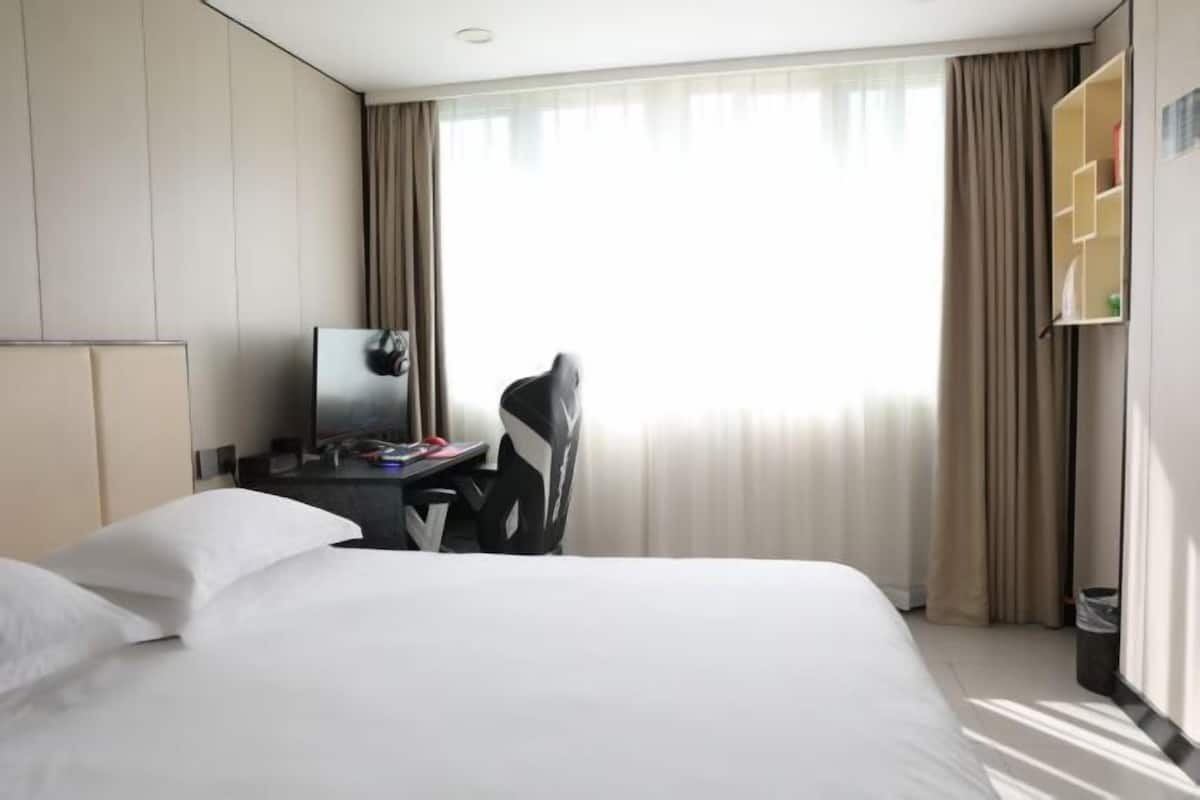 Una camera d'albergo con un letto, una scrivania, una sedia, una televisione e una finestra con tende.