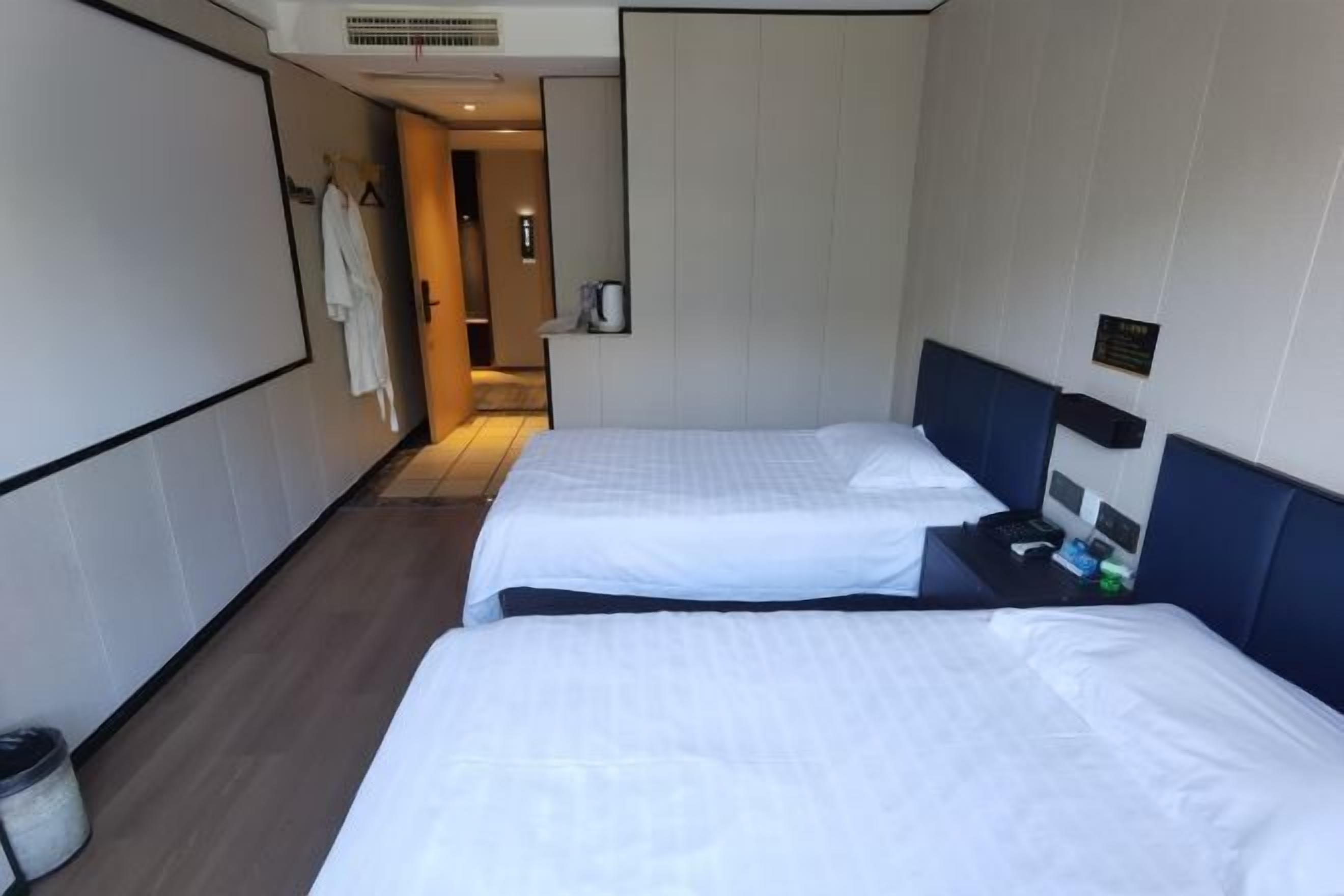 A hotel room with two beds, a small table, a trash bin, and a bathroom door.