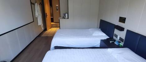 A hotel room with two beds, a small table, a trash bin, and a bathroom door.