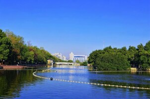 A calm lake with a bridge, surrounded by trees and buildings in the background.