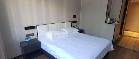 Une chambre d’hôtel équipée d’un lit, d’une table de chevet, de lampes fixées au mur et d’un miroir.