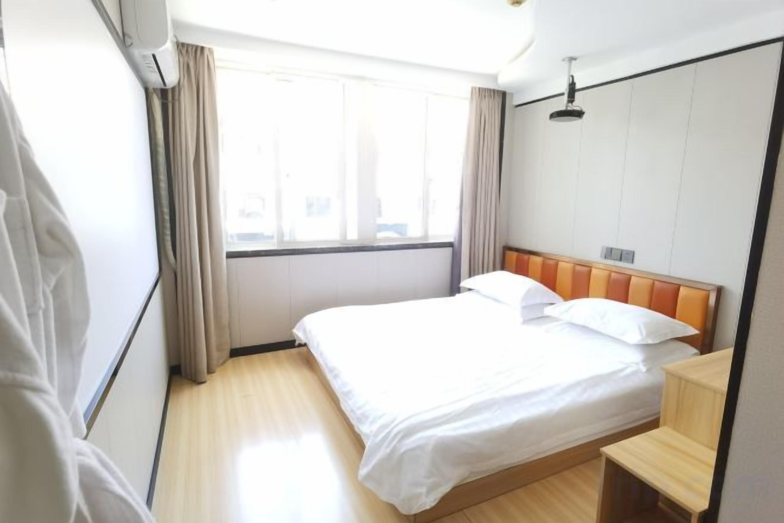 Une chambre d’hôtel avec un lit, une fenêtre, des rideaux et une table de chevet en bois.