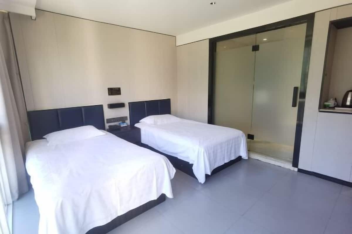 Una camera d'albergo con due letti singoli, un armadio con porta scorrevole in vetro e un piccolo comodino.