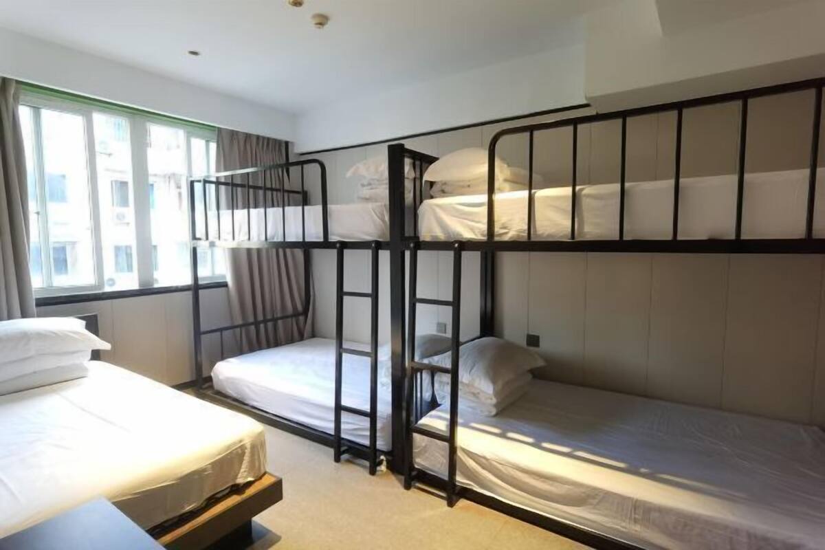 Una camera del dormitorio con letti a castello, una finestra con tende e un letto con testiera in legno.