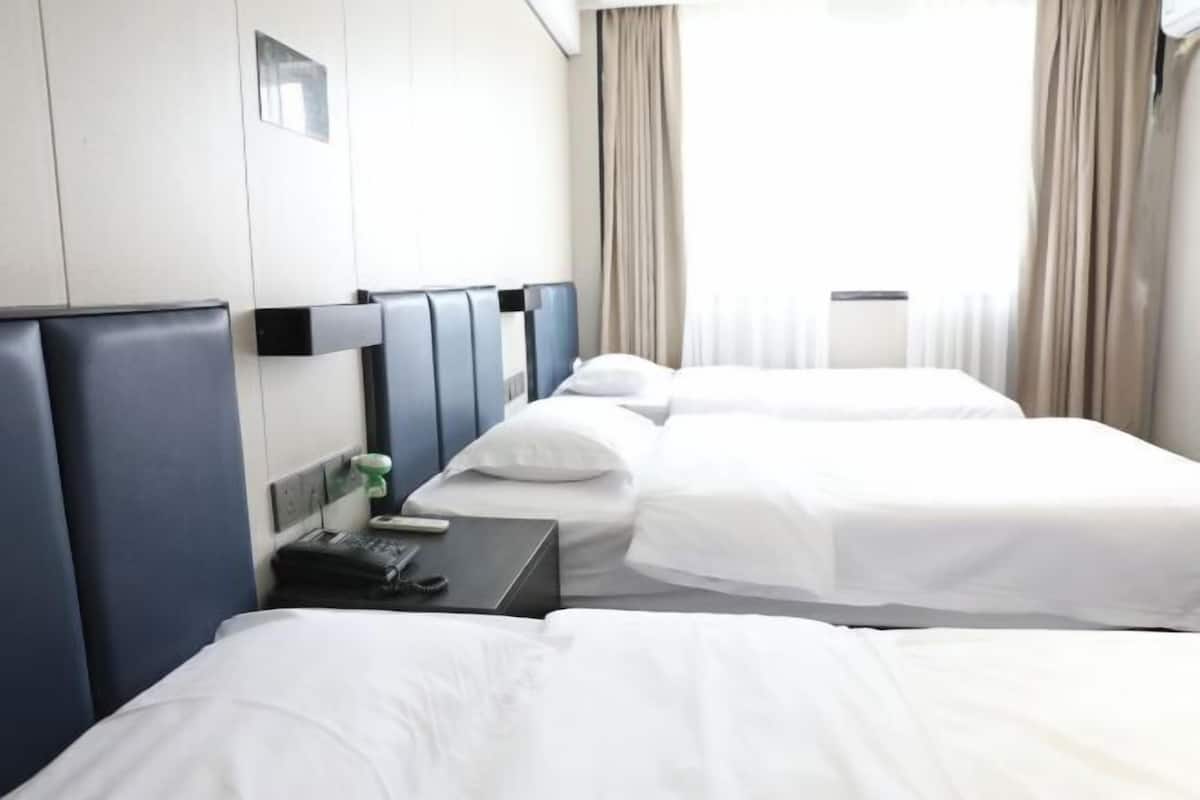 Una camera d'albergo con due letti, un comodino con un telefono e un oggetto verde, e una finestra con tende.
