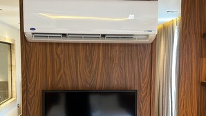 A modern living room with a flat-screen TV mounted on a wooden wall, an air conditioning unit above it, and a wooden cabinet below. - Gaia Pyramids View INN (Giza)