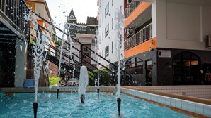 Una piscina con múltiples chorros, rodeada de edificios de varios pisos con balcones y zonas de estar al aire libre.