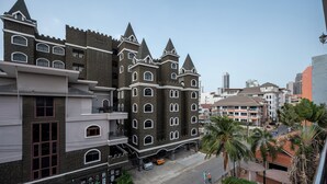Un edificio parecido a un castillo, con múltiples torres y ventanas arqueadas, junto a una calle con palmeras y coches estacionados.