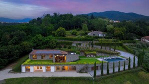 A modern house with a swimming pool, surrounded by lush greenery and hills in the background.